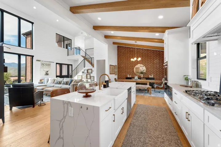 Open-concept interior with exposed wood beams, wood-finish flooring, and a contemporary kitchen featuring a large island with a farmhouse sink