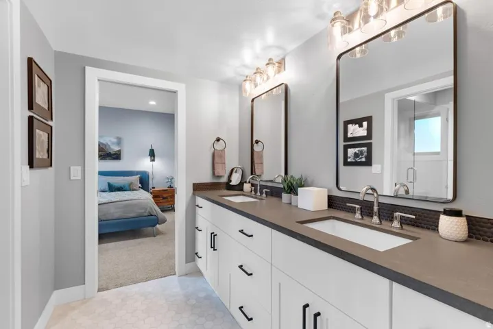 Dual vanity with integrated sinks, dark countertops, white cabinetry, and hexagon tile flooring