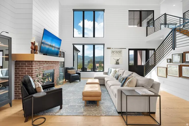 Two-story living area featuring a brick fireplace with a wood mantel, high ceilings with shiplap walls, a multi-level staircase with metal railings, and large black-framed windows
