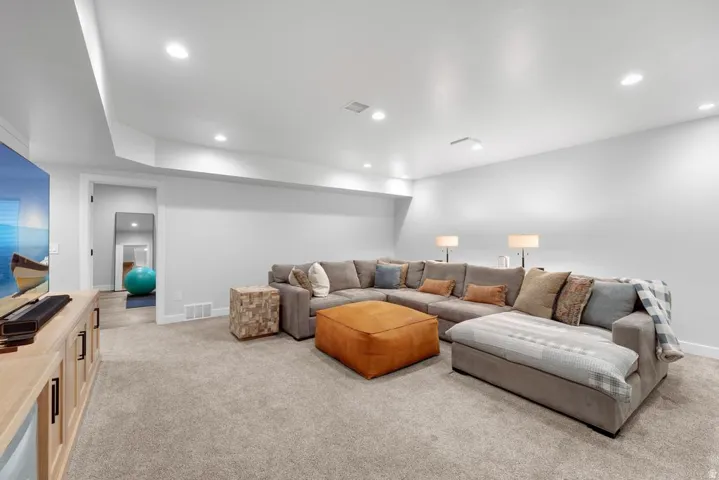 Recessed lighting, light-toned carpeting, built-in media console with cabinet storage, white walls, and a doorway with wood-finish flooring beyond