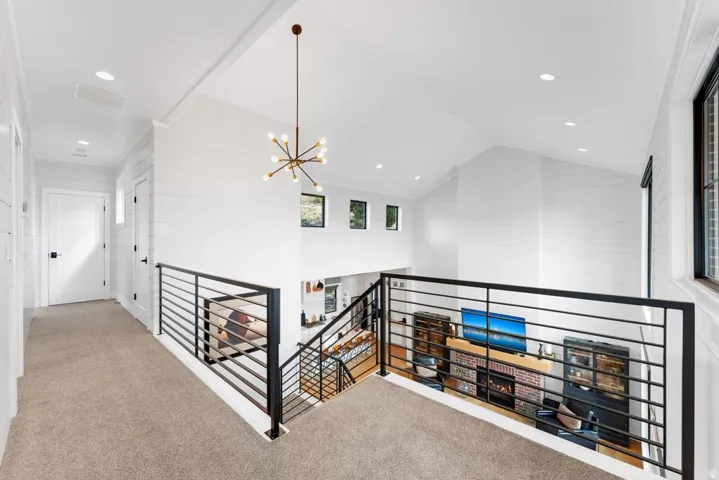 Vaulted ceiling with a contemporary chandelier, shiplap wall accents, black metal horizontal bar railing, recessed lighting, and carpeted flooring