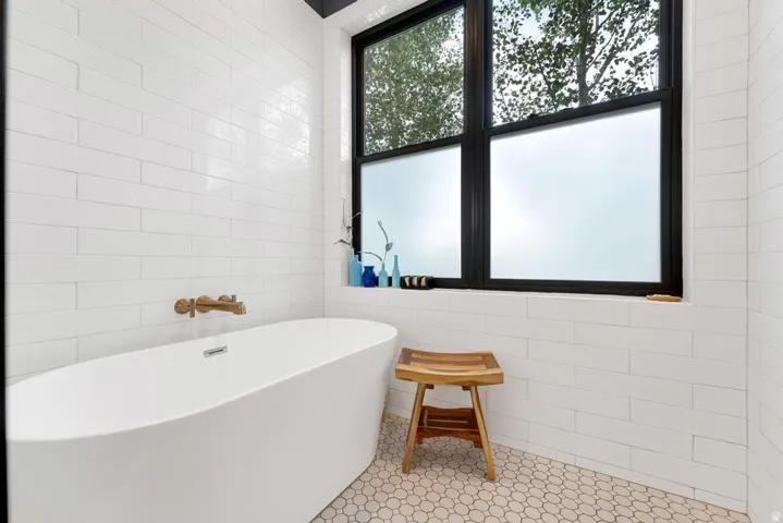 Freestanding soaking tub with wall-mounted bronze-finish faucet, white subway tile walls, and hexagon tile flooring
