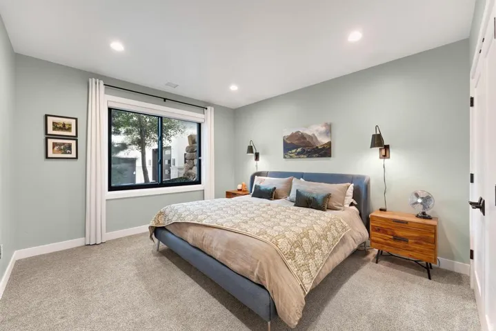 Recessed ceiling lighting, light gray wall paint, large window with white trim, gray carpet flooring, and white paneled doors with black hardware