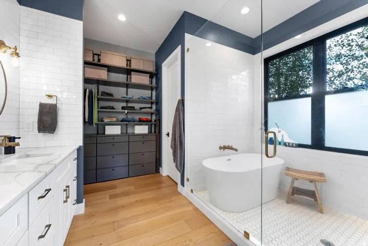 Spacious bathroom featuring a freestanding tub, glass-enclosed shower, dual vanity with a stone countertop, and custom built-in closet storage