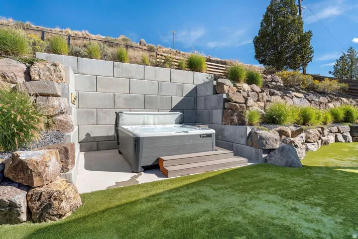Integrated hot tub with composite steps, surrounded by block and natural stone retaining walls, and artificial turf