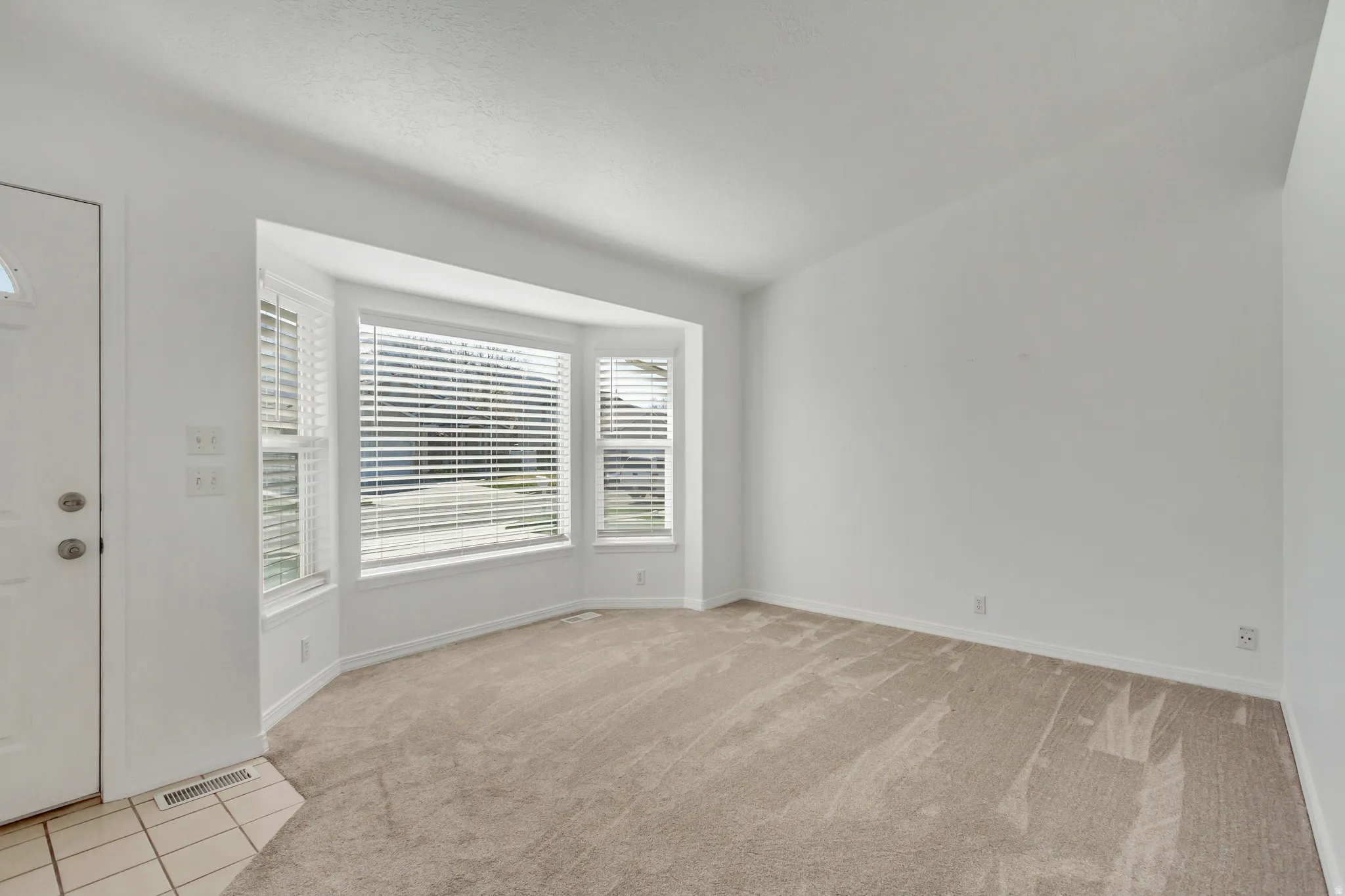 Bay window with horizontal blinds, neutral carpet, and white walls
