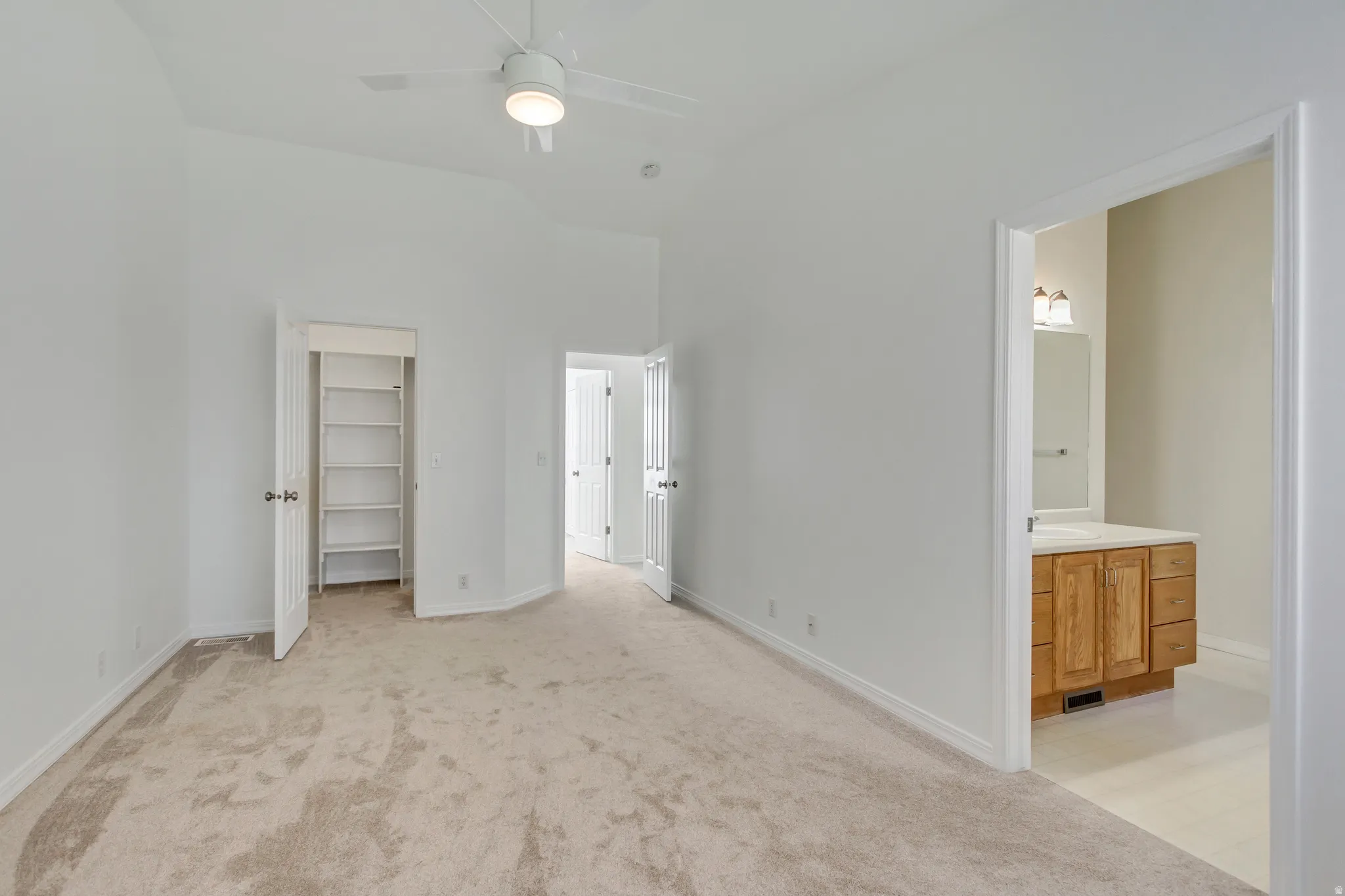 Vaulted ceiling with a ceiling fan, carpet flooring, a built-in closet with shelving, and a wood-finish vanity with a countertop in the bathroom