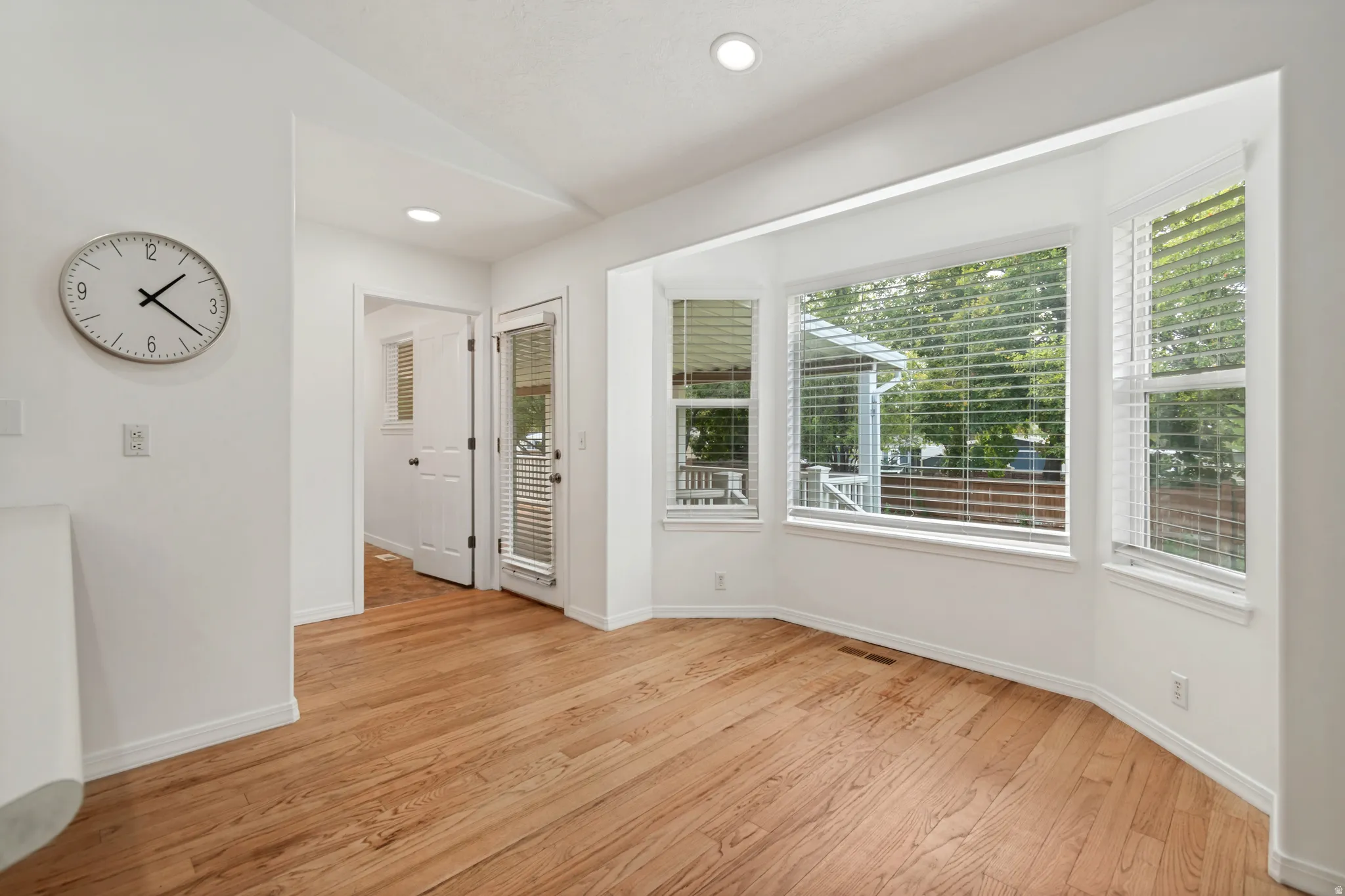 Hardwood flooring throughout, recessed ceiling lighting, bay window with blinds, white trim, and a glass-paneled exterior door