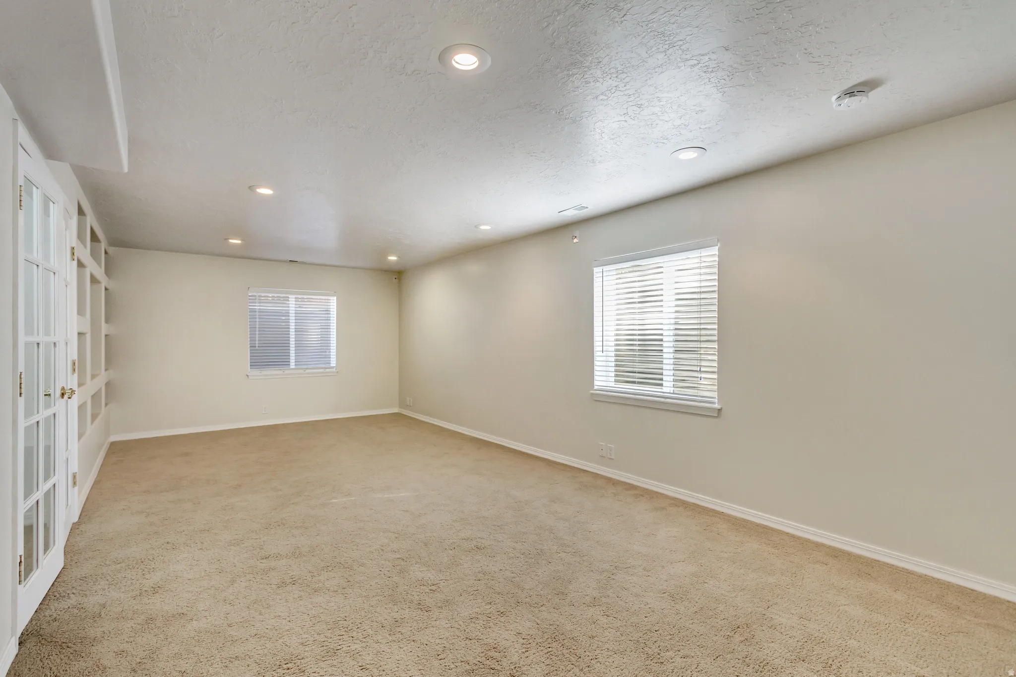 Carpeted room featuring recessed lighting, multiple windows with blinds, and white French doors opening to built-in shelving