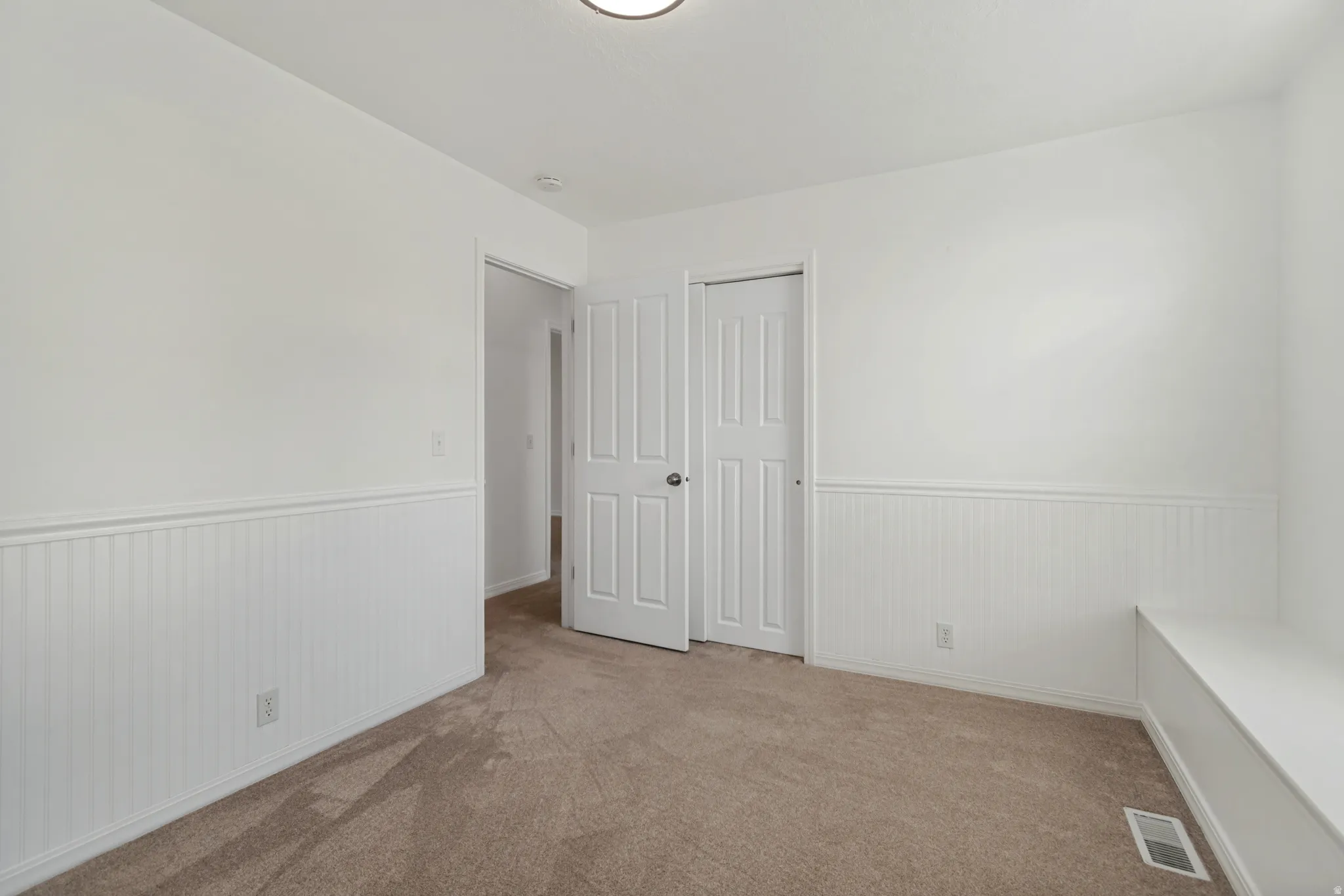 Neutral wall paint with wainscoting detail, carpet flooring, and a built-in bench