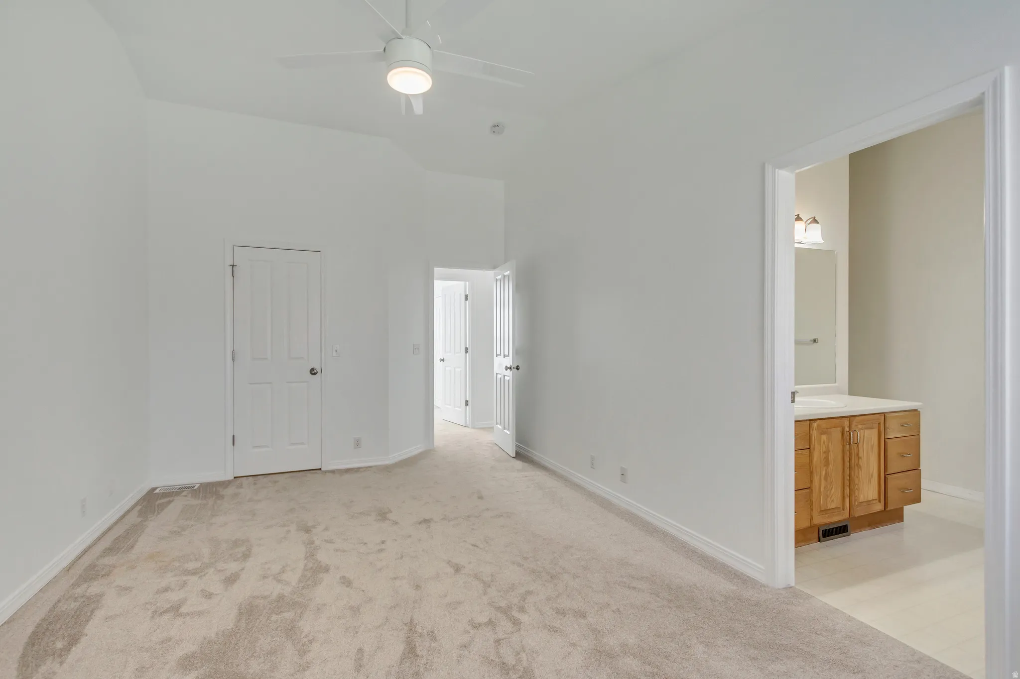 Vaulted ceiling, white ceiling fan with integrated lighting, carpeted flooring, light wood-finish vanity with countertop, and wall-mounted vanity lighting