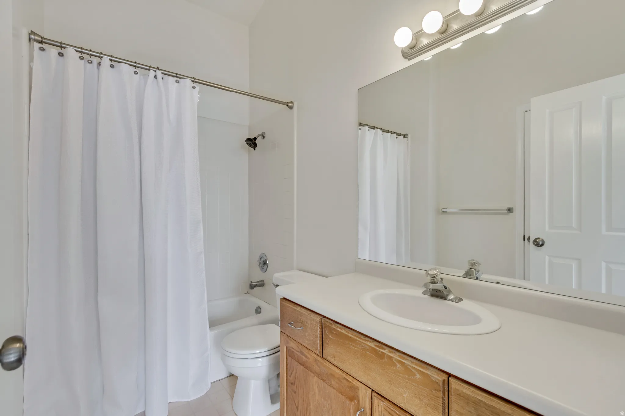 Bathtub with a shower fixture, wood-finish vanity with an integrated sink, broad wall-mounted mirror, and overhead vanity lighting