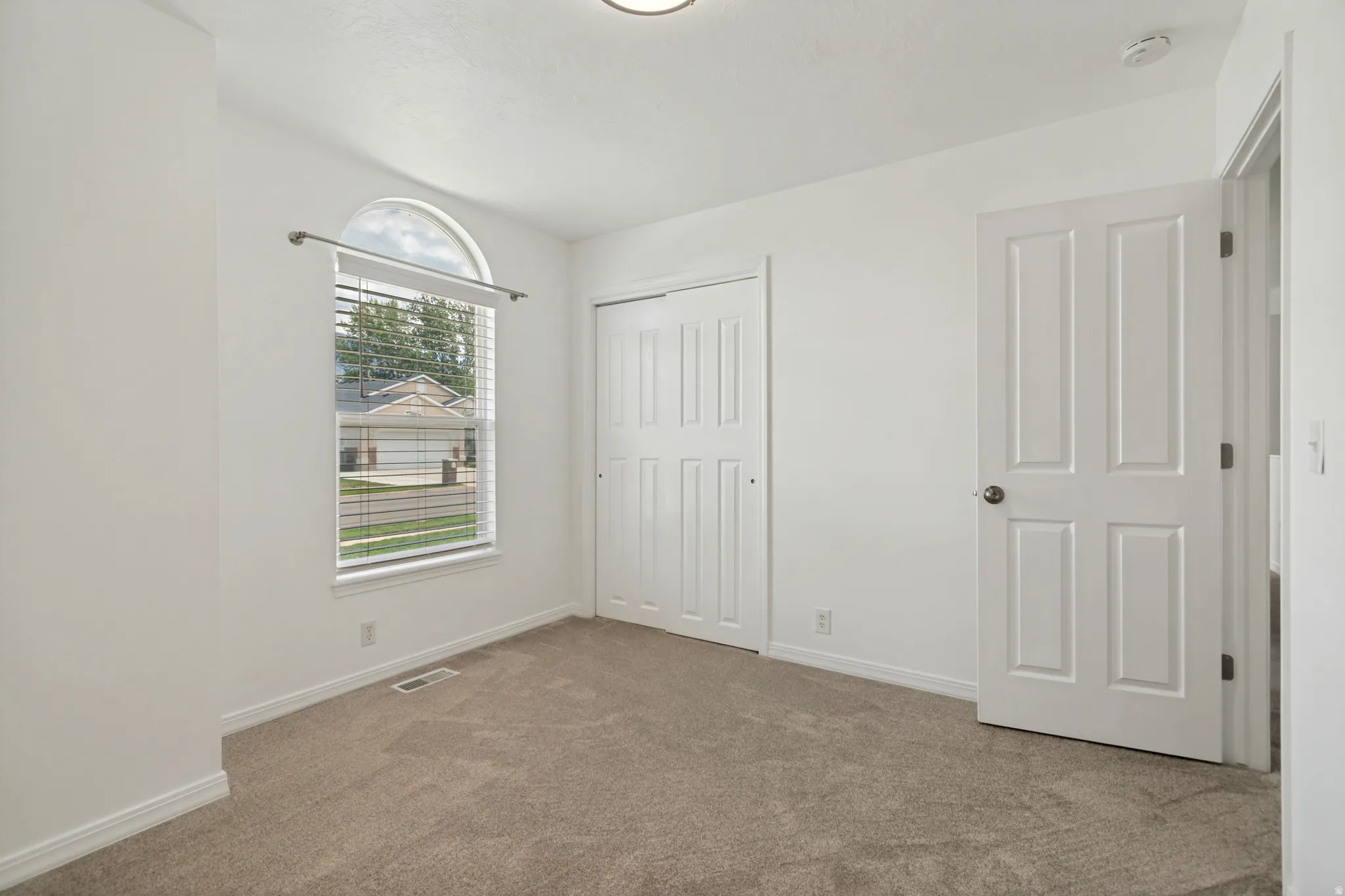 Arched window with blinds, wall-to-wall carpeting, and a closet with bifold doors