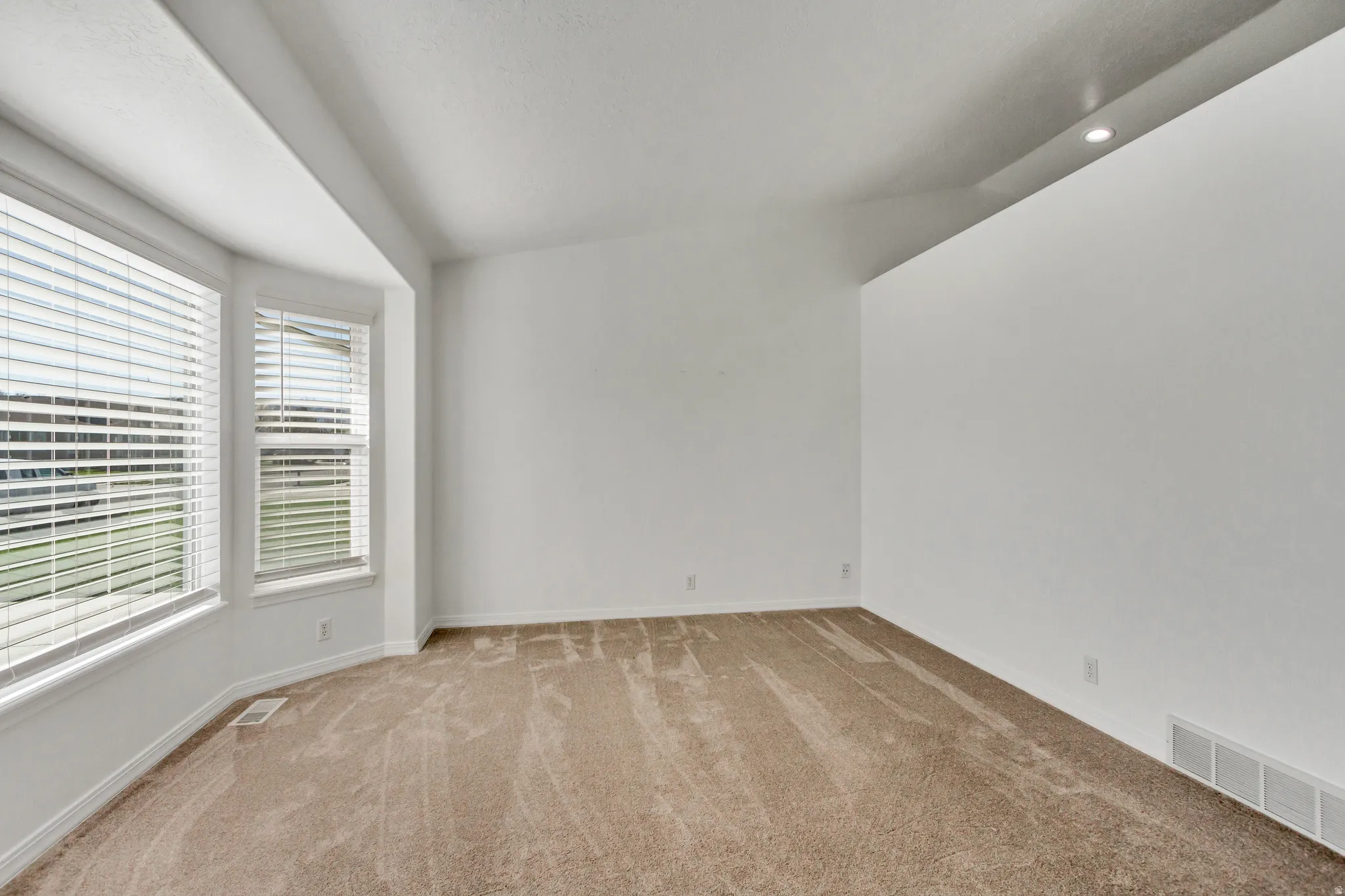 Carpeted room with a bay window, natural light, and a sloped ceiling featuring a recessed light