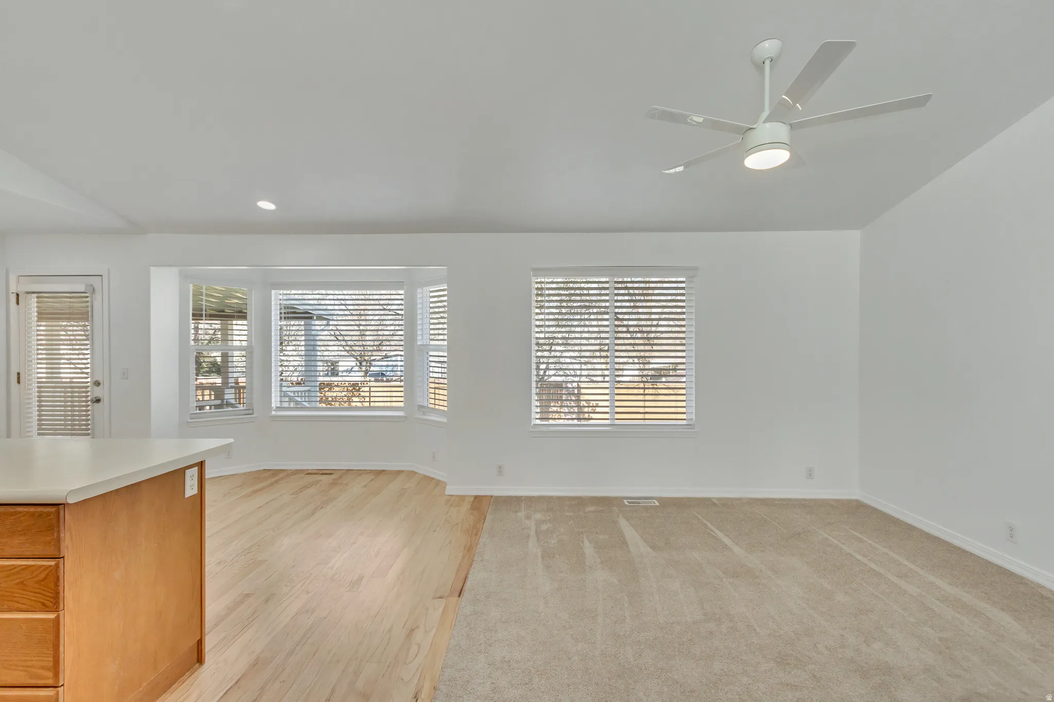 White walls with a ceiling fan, light wood-finish flooring, and a bay window