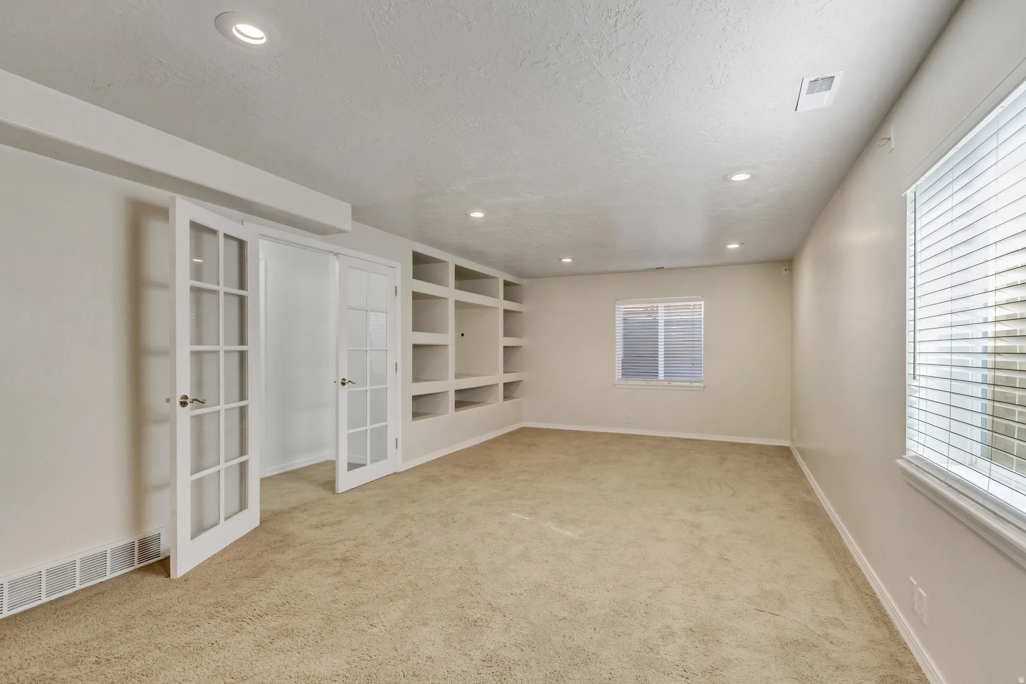 Recessed lighting, built-in shelving, glass-paneled French doors, and two windows with blinds
