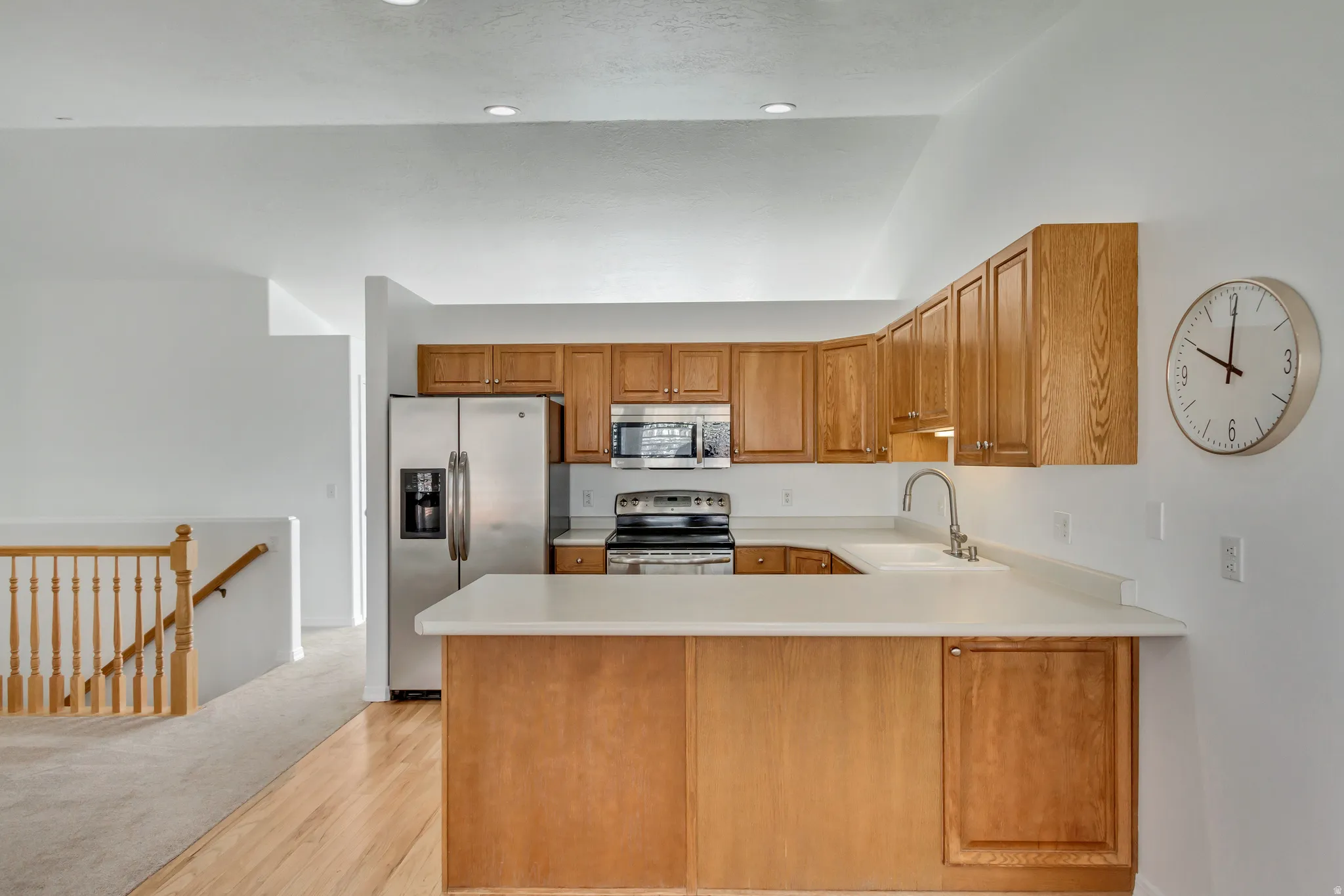 Kitchen featuring wood cabinetry, light-toned countertops, stainless steel appliances, and a stainless steel sink with a gooseneck faucet