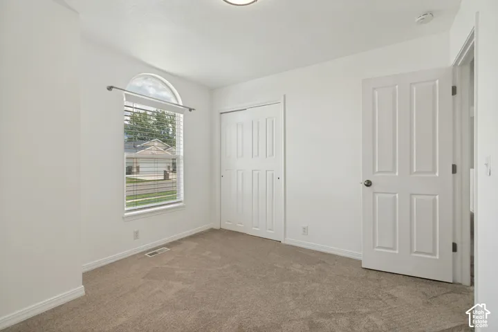 Arched window with blinds, wall-to-wall carpeting, and a closet with bifold doors