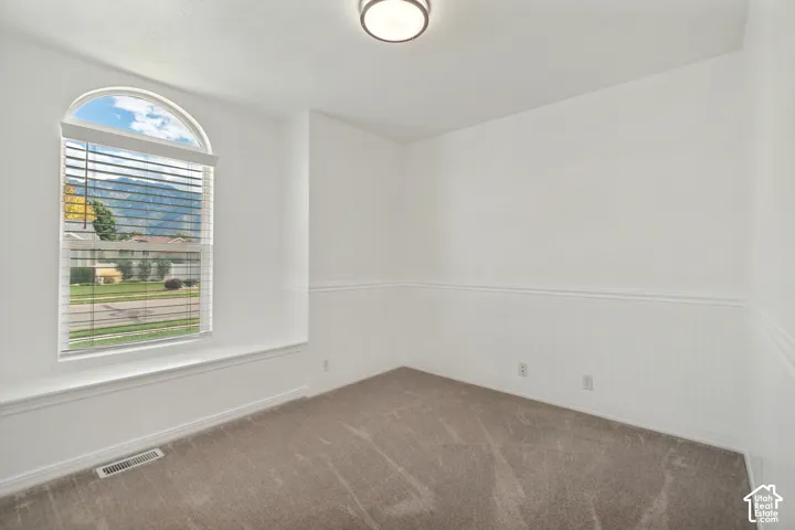 Arched window with blinds, carpeted flooring, wainscoting, and a flush mount ceiling light