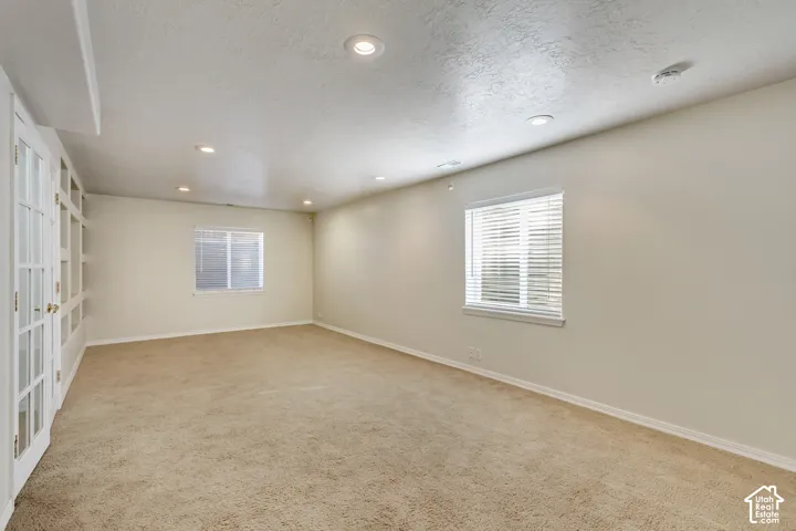 Carpeted room featuring recessed lighting, multiple windows with blinds, and white French doors opening to built-in shelving