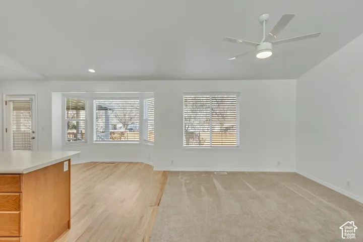 White walls with a ceiling fan, light wood-finish flooring, and a bay window