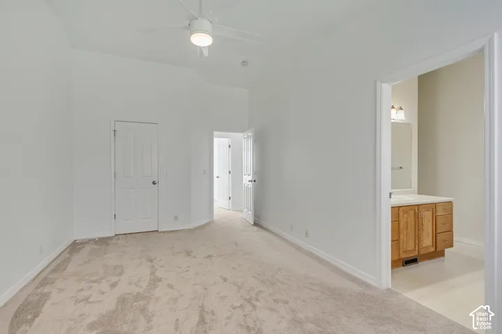 Vaulted ceiling, white ceiling fan with integrated lighting, carpeted flooring, light wood-finish vanity with countertop, and wall-mounted vanity lighting