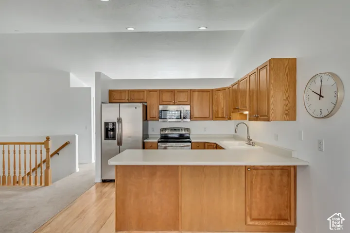 Kitchen featuring wood cabinetry, light-toned countertops, stainless steel appliances, and a stainless steel sink with a gooseneck faucet