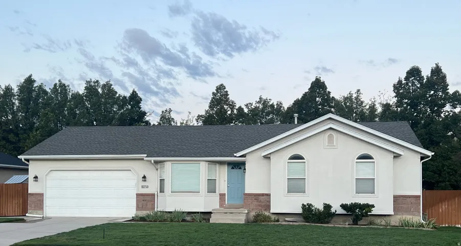 Ranch-style exterior with a dark shingle roof, attached garage, light stucco siding, and a blue entry door