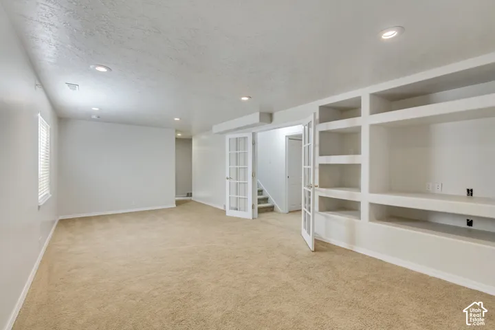 Recessed lighting, built-in shelving, built-in media console, French doors, and neutral carpeting