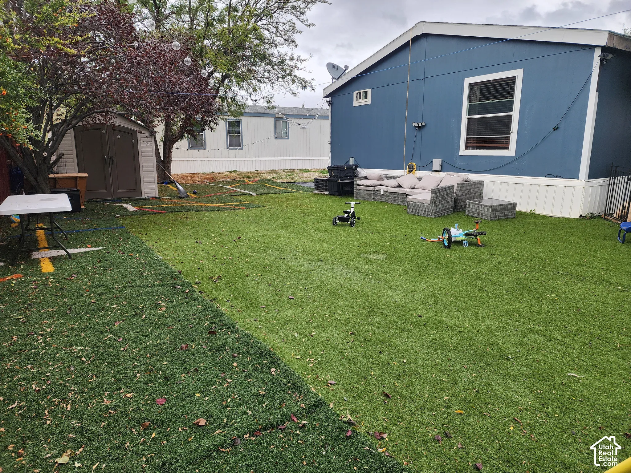Backyard featuring synthetic turf, a detached storage shed, and mature trees