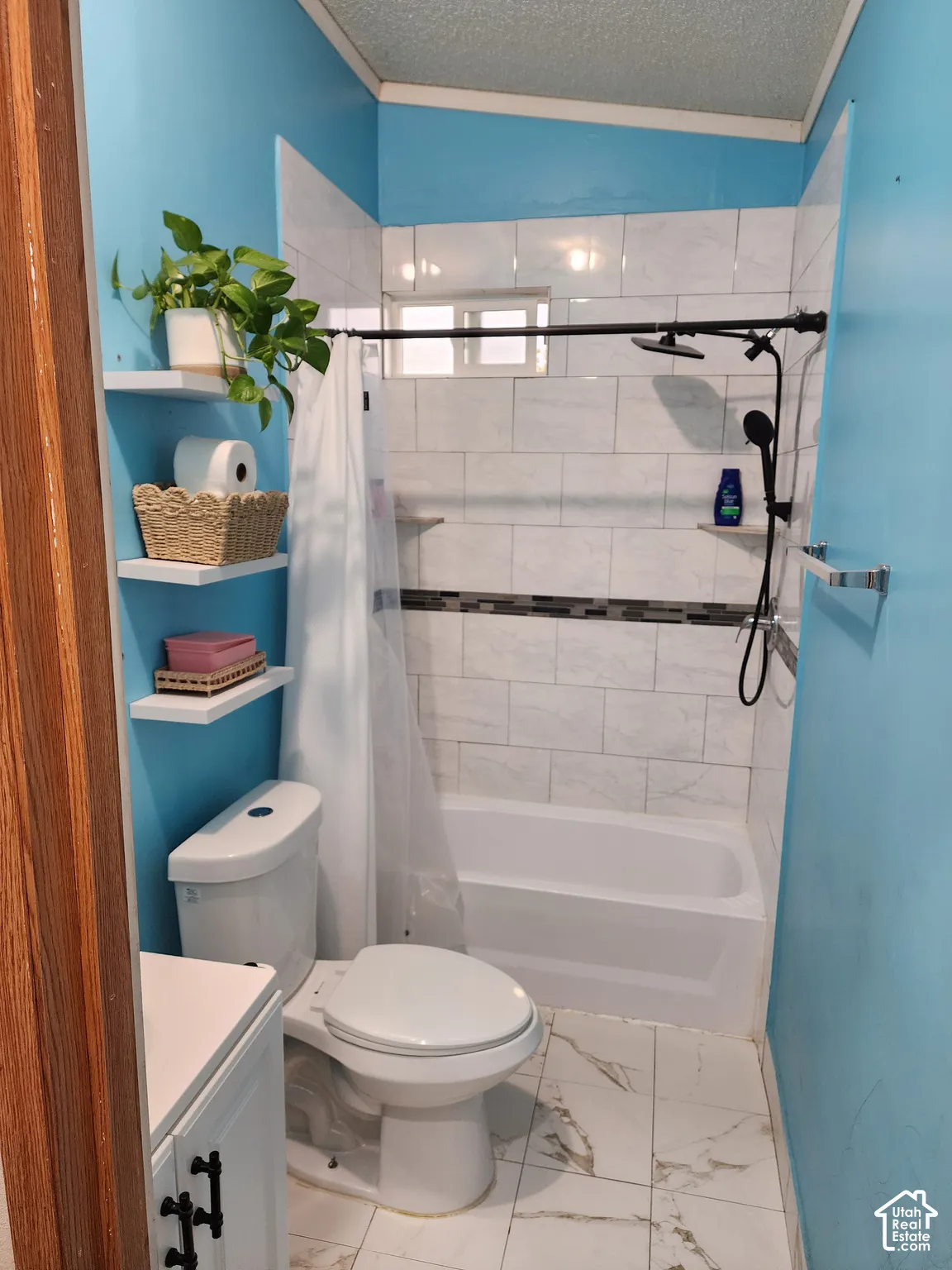 Bathroom featuring white tile flooring, built-in wall shelving, a tub-shower combination with decorative tile inlay, and a matte black rainfall showerhead