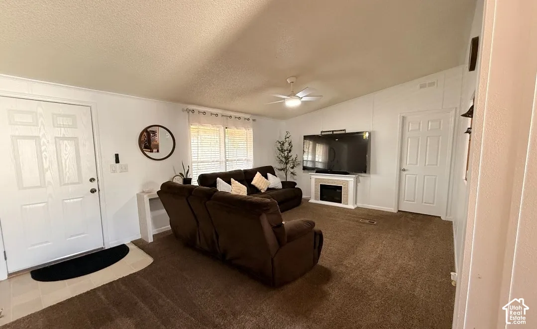 Vaulted ceiling, ceiling fan with integrated lighting, built-in electric fireplace, white paneled doors, and large windows with blinds