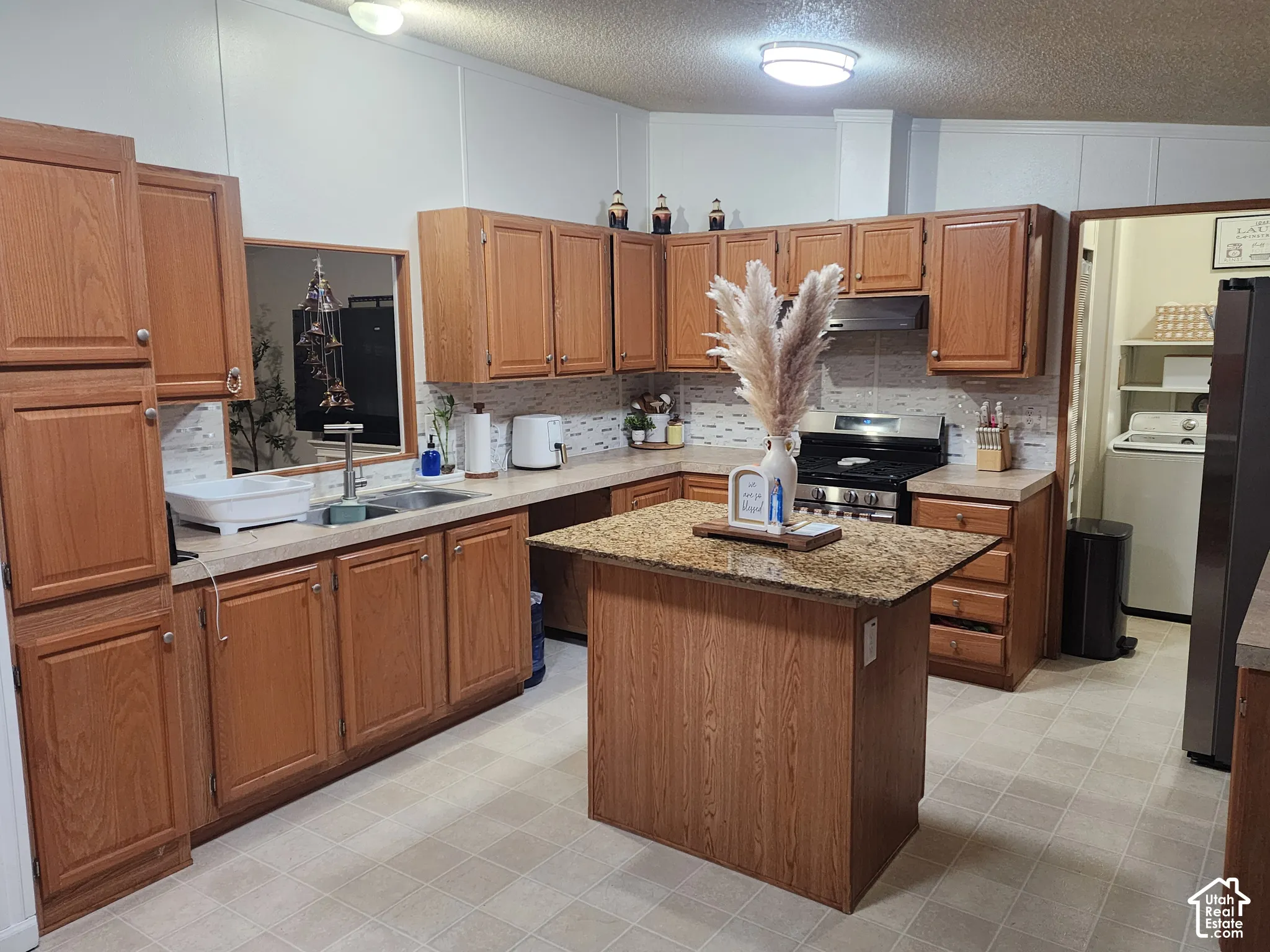Kitchen featuring wood cabinetry, stone-finish countertops, center island, integrated stainless steel range, and tile backsplash