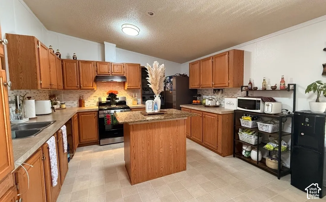 Kitchen featuring wood-finish cabinetry, a central island with a stone-finish countertop, stainless steel appliances, and a mosaic tile backsplash