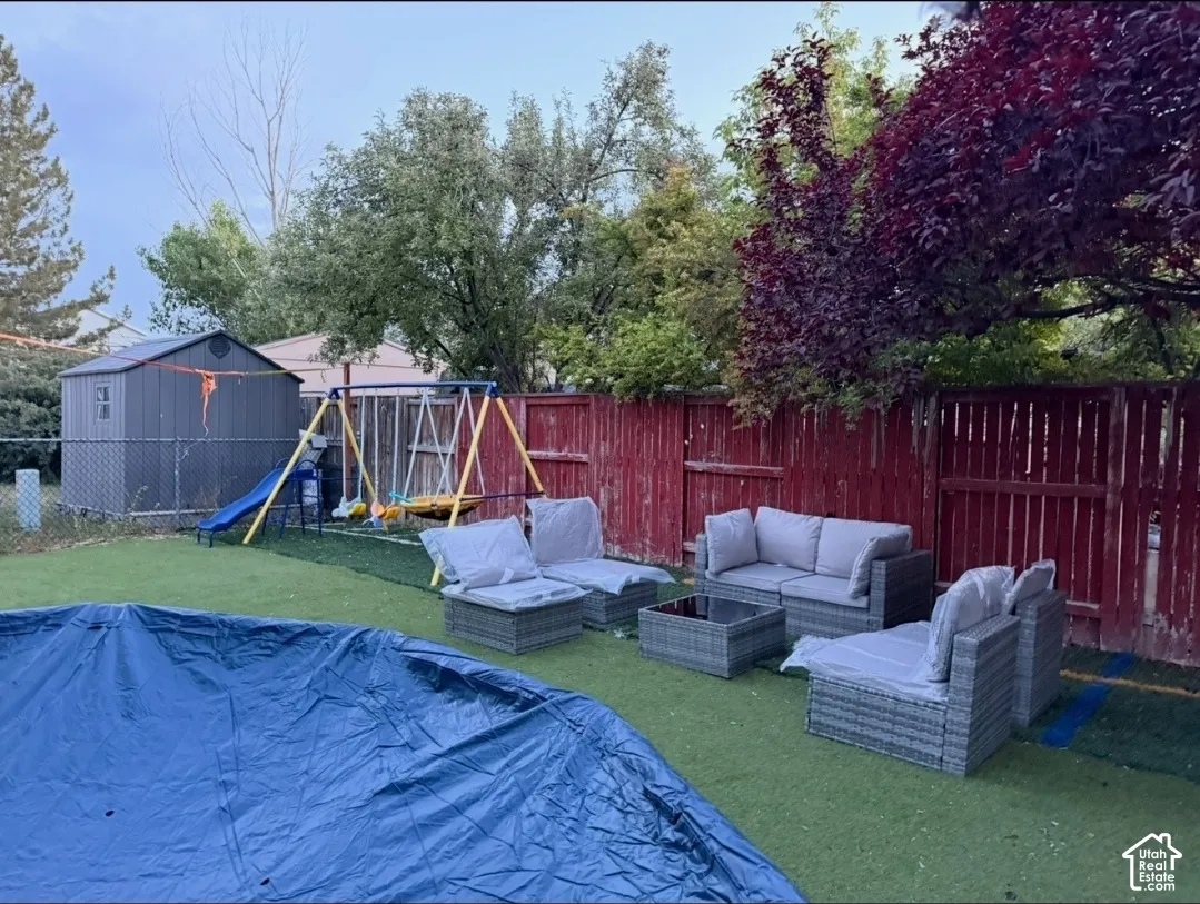 Fenced backyard with artificial turf, featuring a storage shed and mature trees