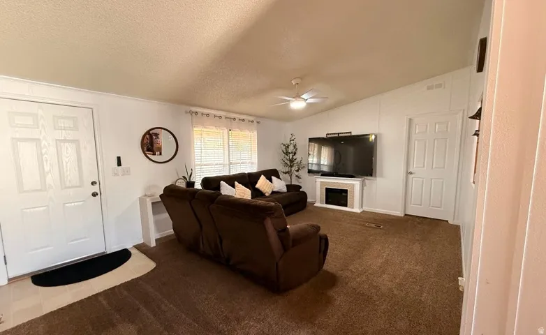 Vaulted ceiling, ceiling fan with integrated lighting, built-in electric fireplace, white paneled doors, and large windows with blinds