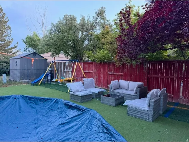 Fenced backyard with artificial turf, featuring a storage shed and mature trees