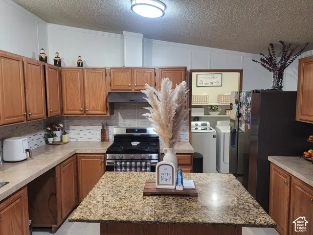 Kitchen featuring wood cabinetry, stone-finish countertops, a central island, tiled backsplash, and stainless steel gas range