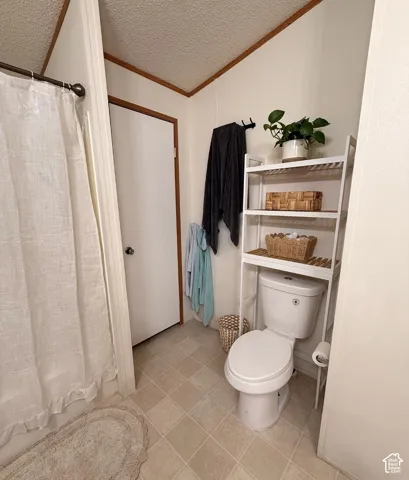 White toilet with an over-the-toilet shelving unit, light-toned square floor tiles, and a privacy door