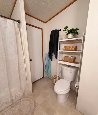 White toilet with an over-the-toilet shelving unit, light-toned square floor tiles, and a privacy door