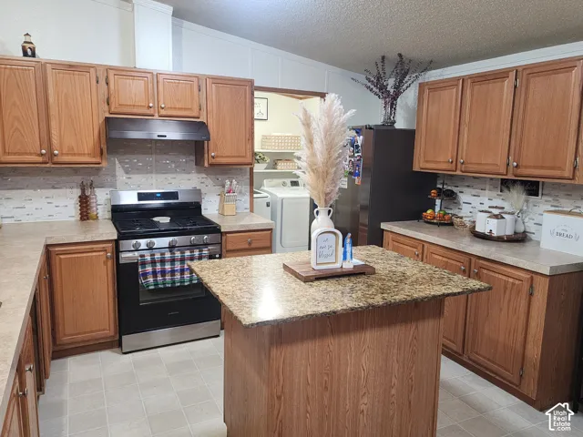Kitchen featuring wood cabinetry, stone-finish countertops, a central island, tiled backsplash, and a gas range
