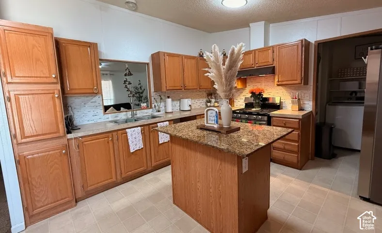 Kitchen featuring wood cabinetry, a central island with a stone-finish countertop, stainless steel appliances, and a tile backsplash