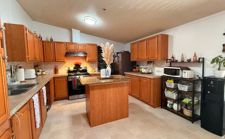 Kitchen featuring wood-finish cabinetry, a central island with a stone-finish countertop, stainless steel appliances, and a mosaic tile backsplash