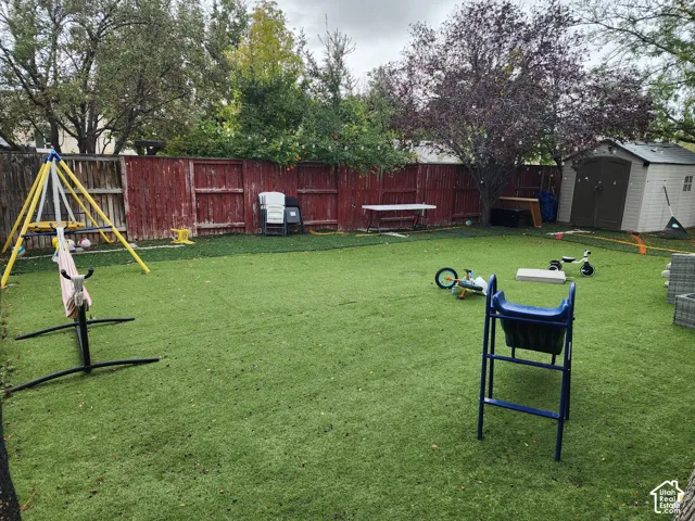 Fenced backyard featuring synthetic turf, mature trees, and a detached storage shed