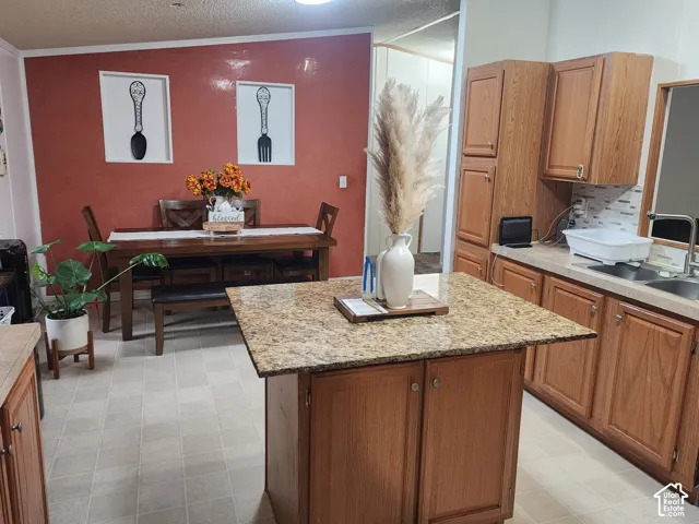 Kitchen featuring wood cabinetry, a center island with a stone-finish countertop, double-basin sink, and decorative tile backsplash