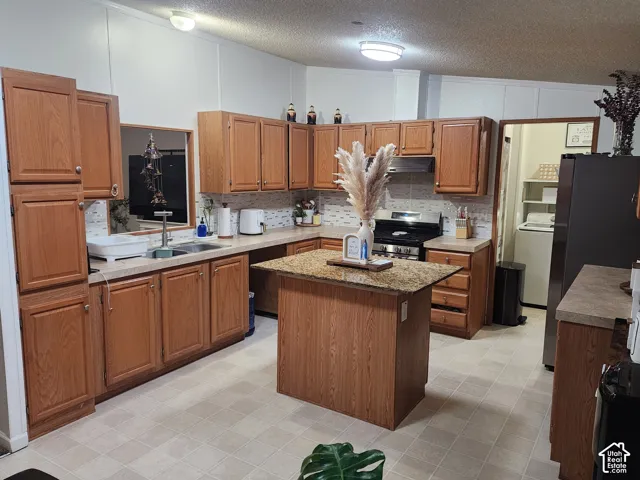 Kitchen featuring wood cabinetry, a central island with a stone-finish countertop, patterned tile backsplash, and flush-mount ceiling lighting