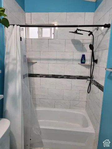 Bathtub enclosure featuring white stone-finish tile surround, a horizontal glass and stone decorative inlay, a matte black dual-head shower system, and built-in corner shelving