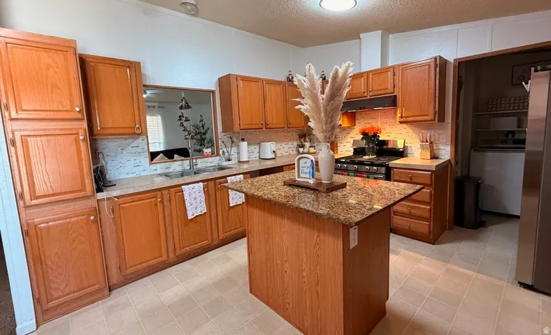 Kitchen featuring wood cabinetry, a central island with a stone-finish countertop, stainless steel appliances, and a tile backsplash