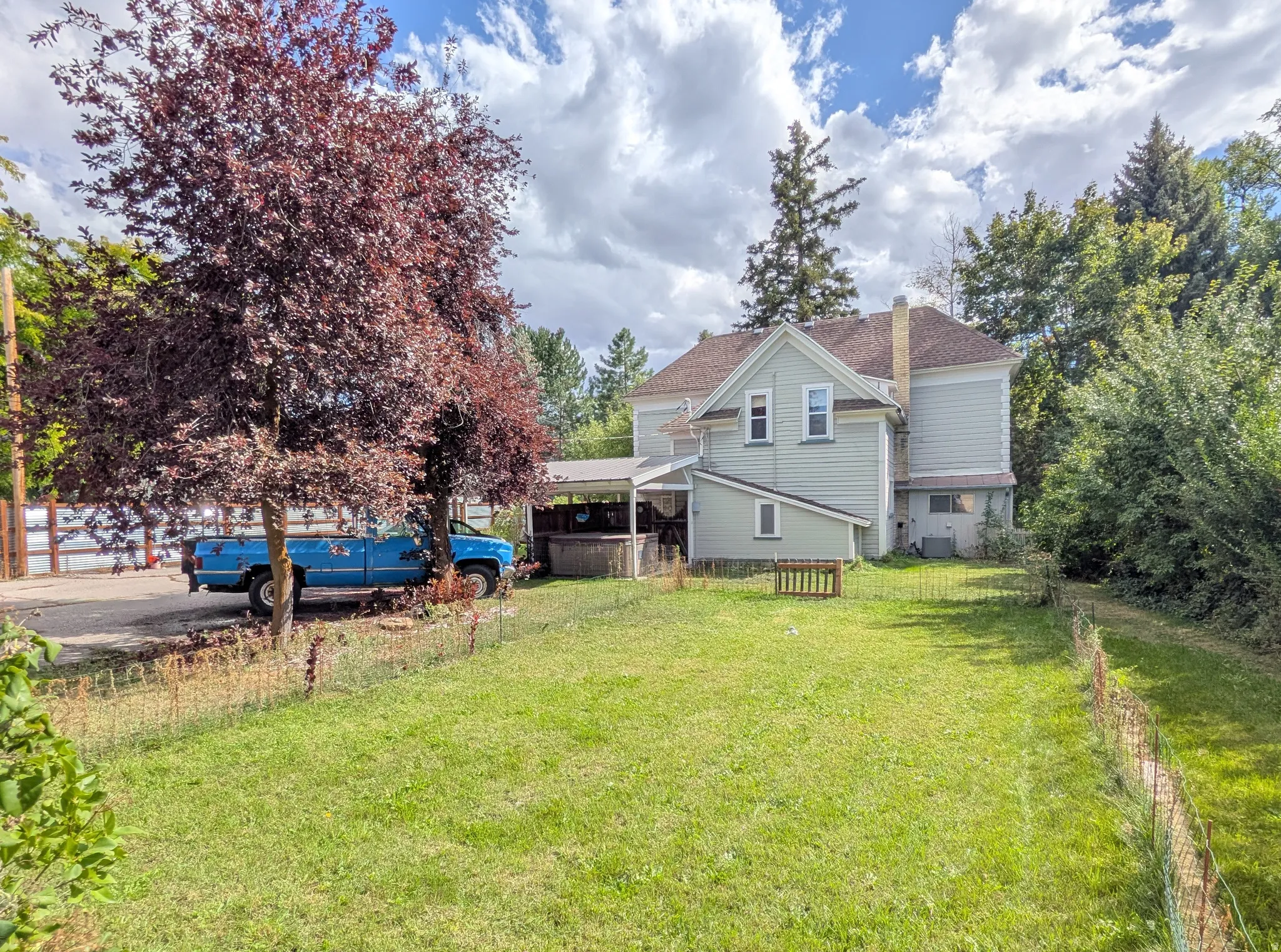 Expansive backyard with a manicured lawn, mature trees, and a covered porch