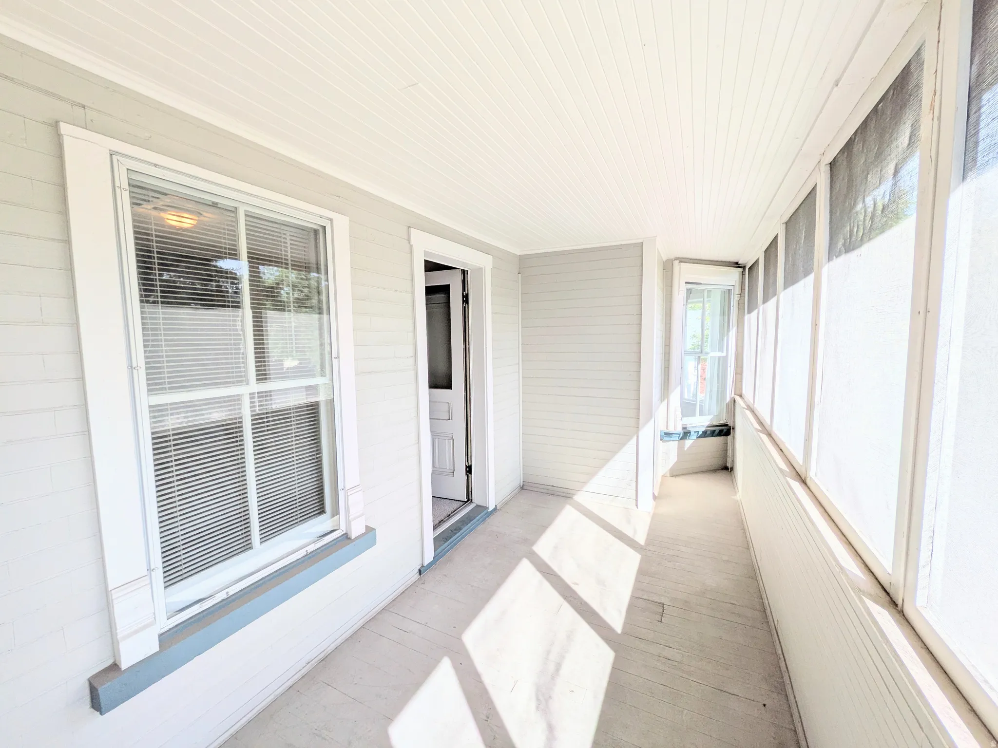 Enclosed porch with beadboard ceiling, wood-finish flooring, and natural light